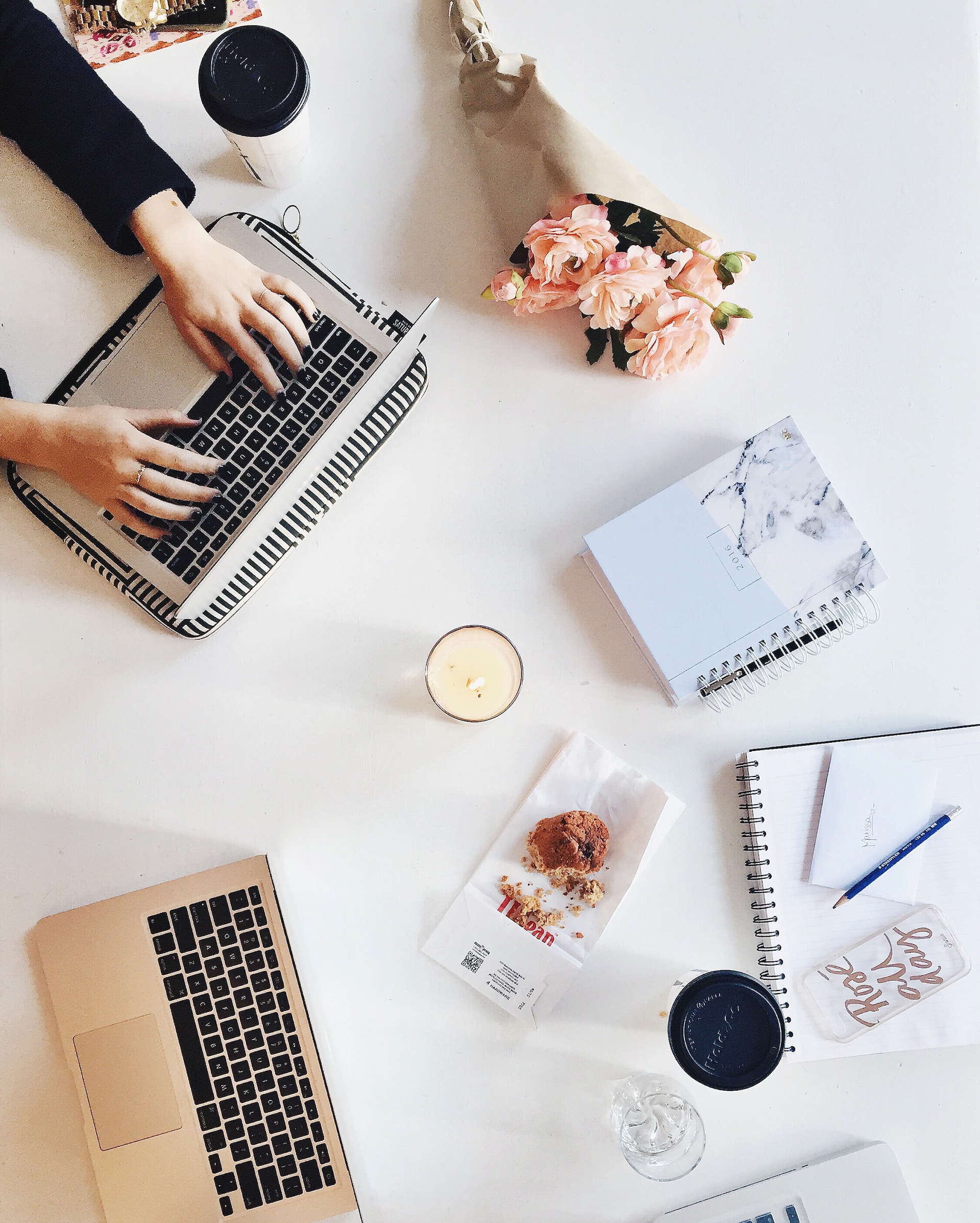 Aerial view on a white desk on which there are 2 laptops, flowers, notebooks and a coffee mug