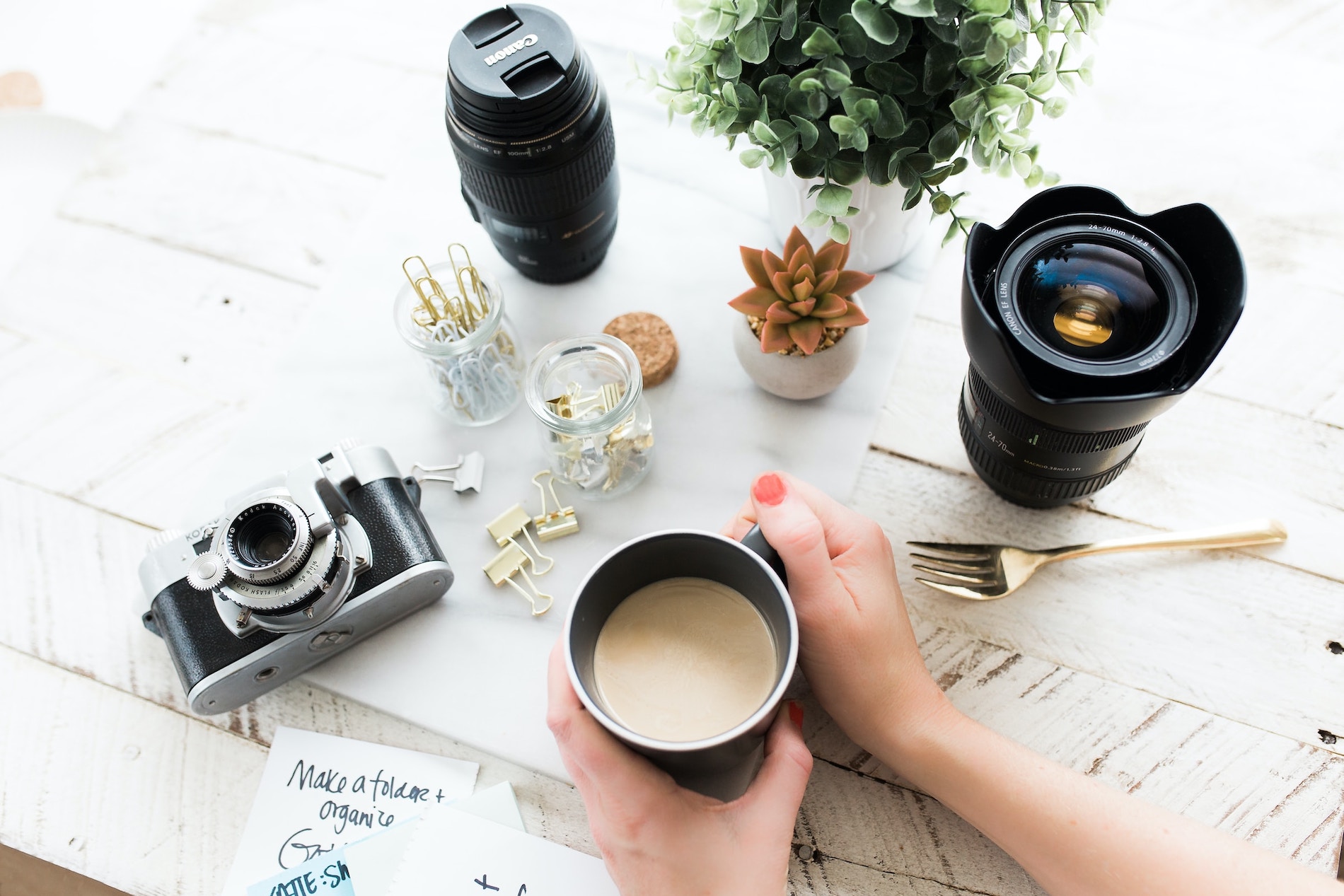 Camera parts spread on a wooden table, female hands holding a coffee mug next to them